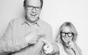 a black and white image of a man and a woman smiling and pointing at each other and the camera
