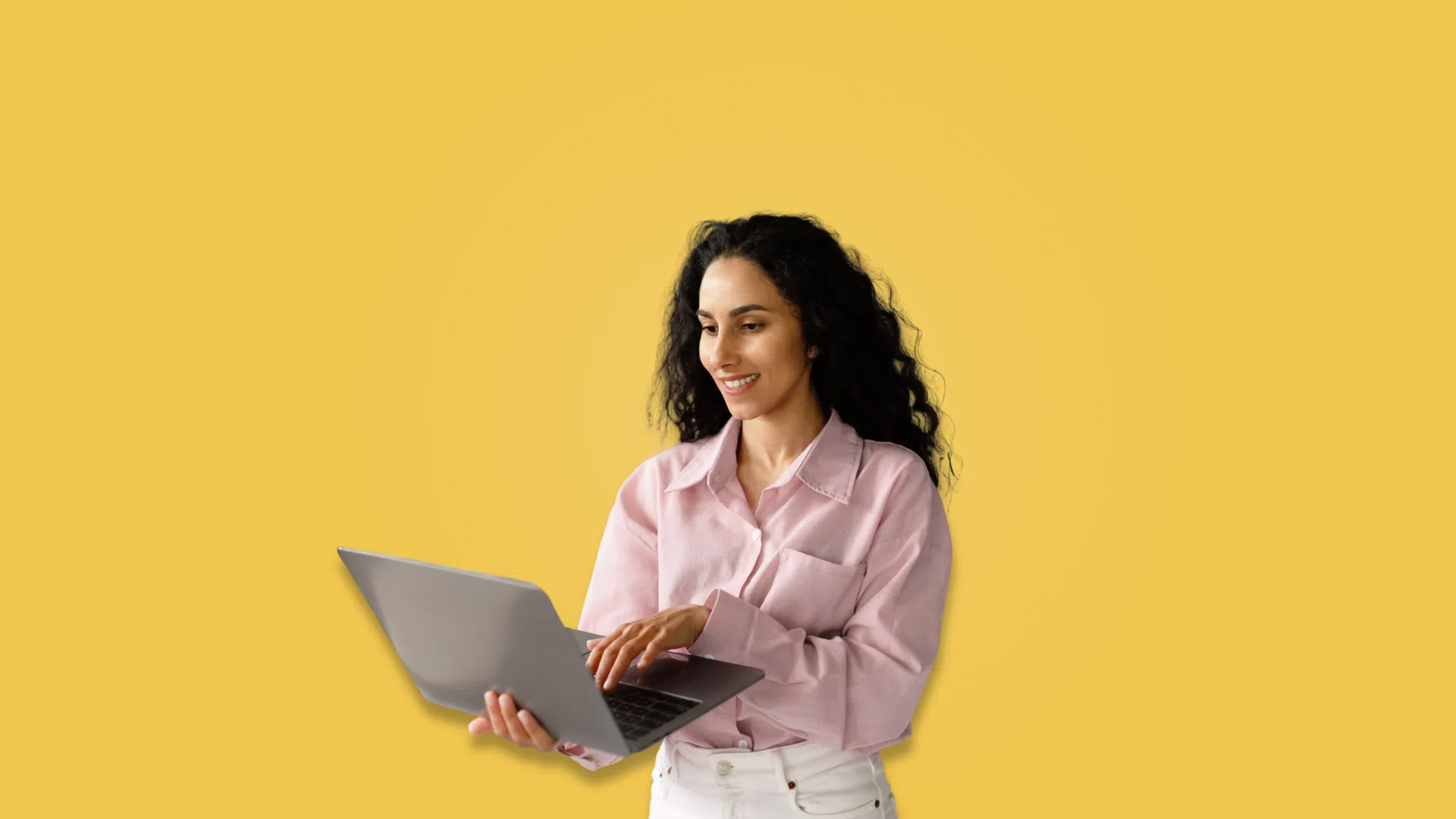A woman with a laptop in hand poses in front of a vibrant yellow background, showcasing her engagement with technology.