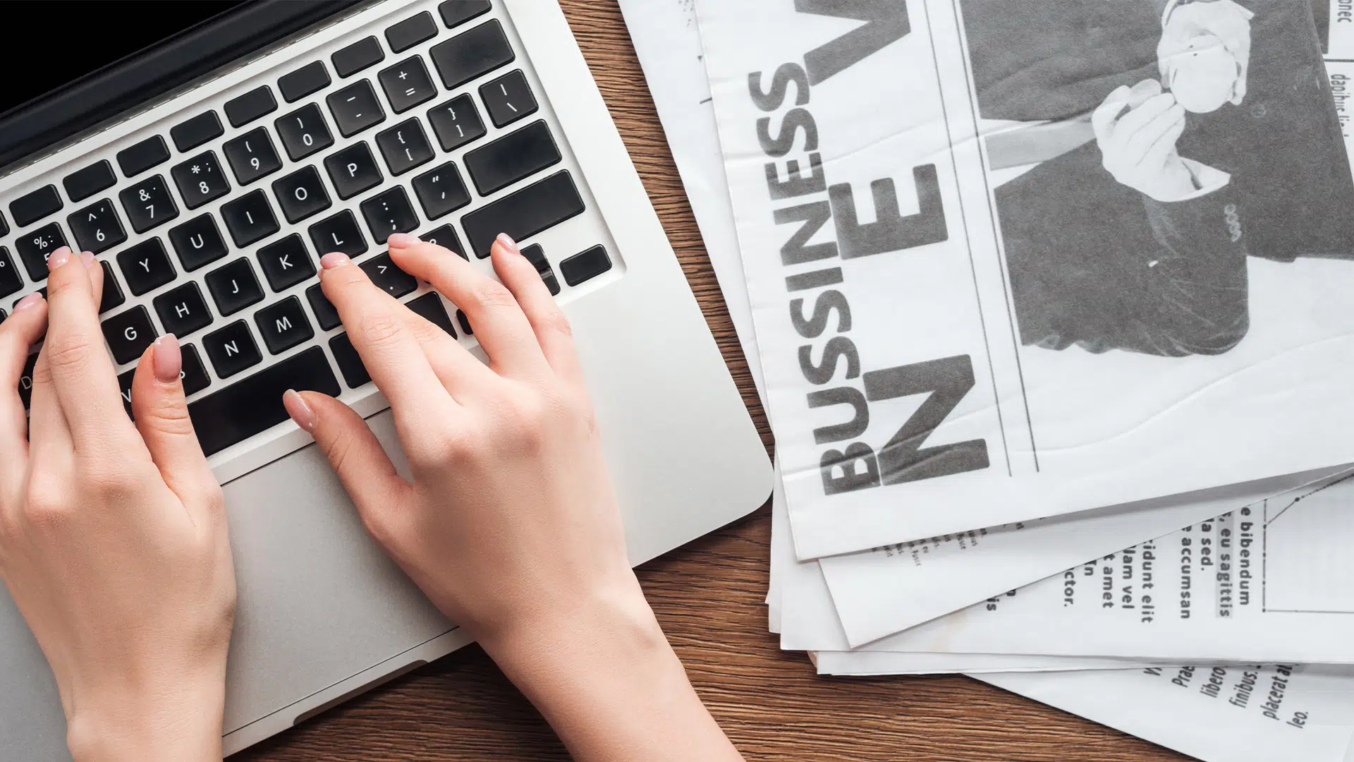 Person typing on a laptop with a newspaper nearby, representing the shift from traditional to digital advertising